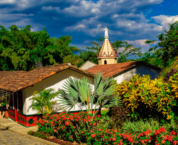 Fachada colorida de una iglesia colonial rodeada de vegetación tropical.