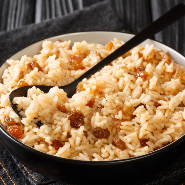 Coconut rice with raisins served in a dark bowl, a traditional preparation of Caribbean cuisine.