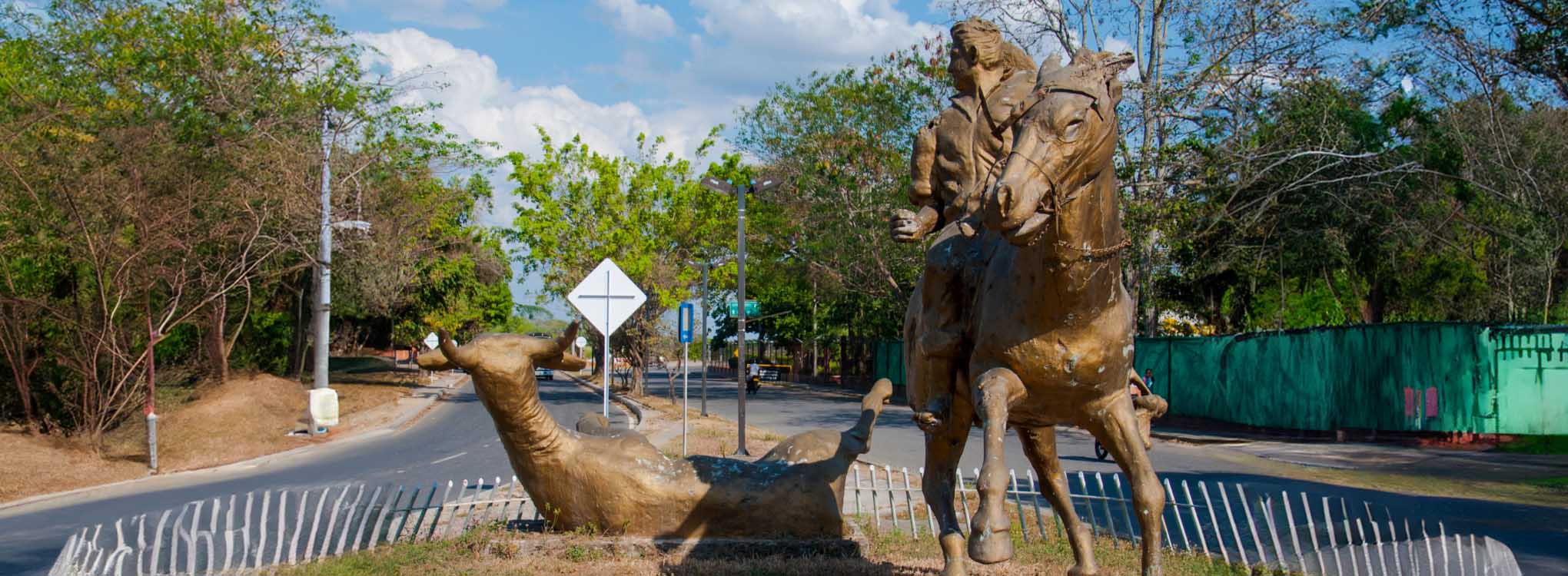 Escultura de un llanero montado a caballo junto a un toro en el suelo.