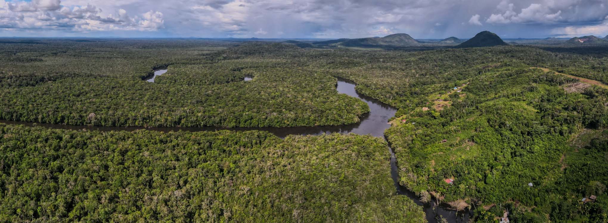 Vista aérea de la selva amazónica con ríos serpenteantes, densa vegetación y colinas en el horizonte.