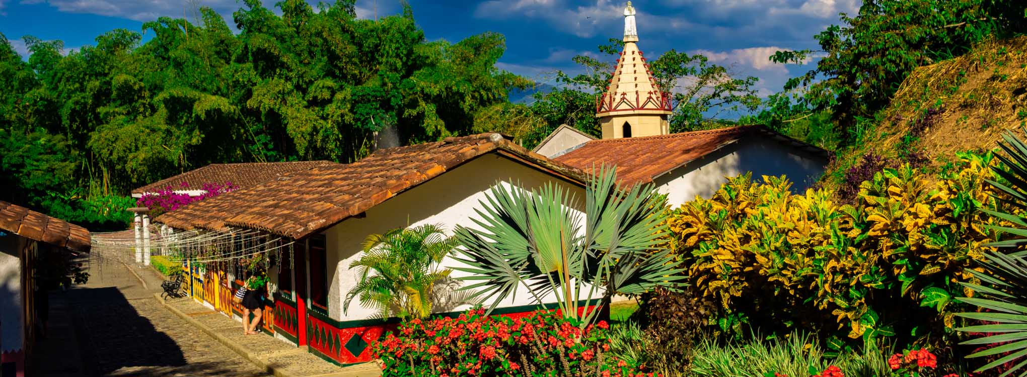 Fachada colorida de una iglesia colonial rodeada de vegetación tropical.