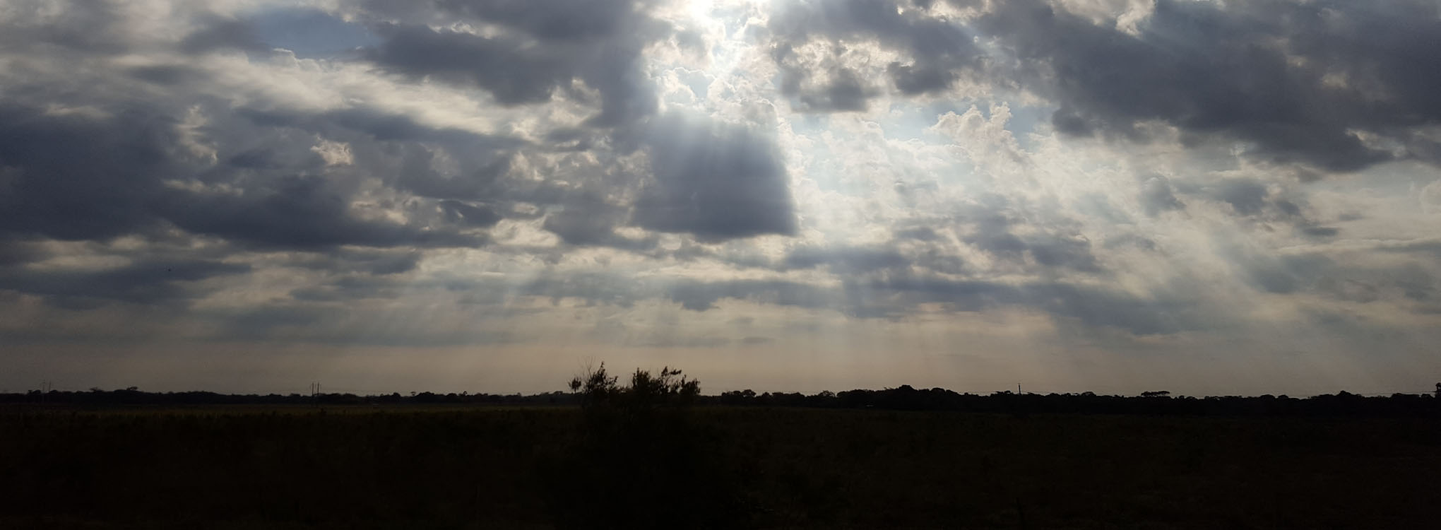 Cielo parcialmente nublado con rayos de sol atravesando las nubes, iluminando ligeramente el paisaje 