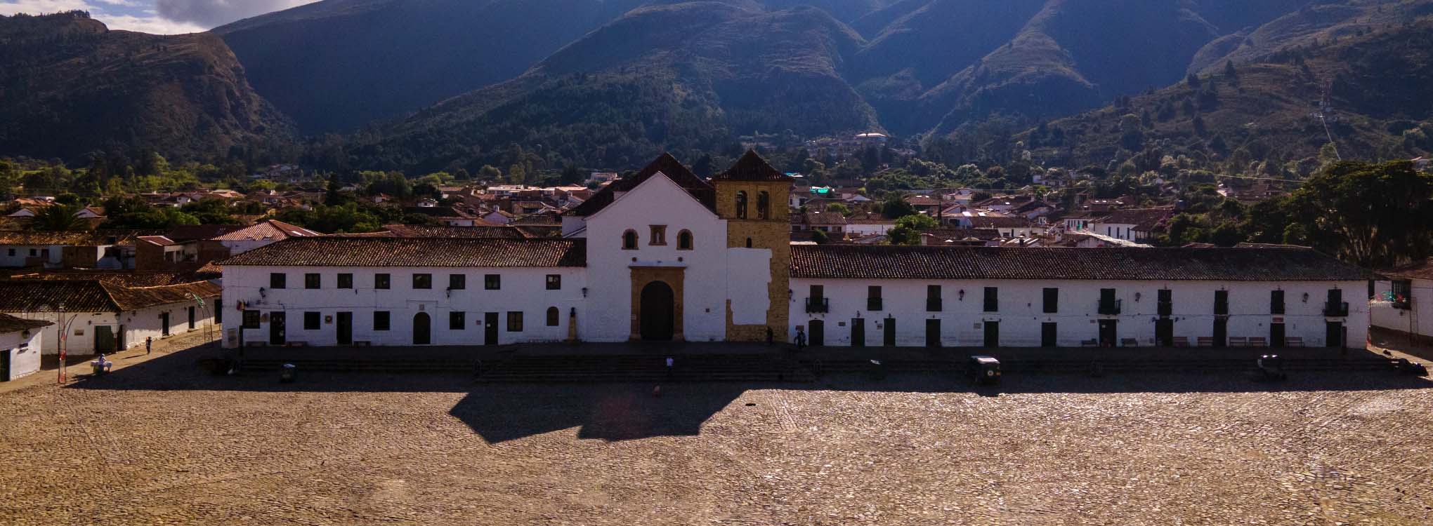 Plaza histórica con una iglesia colonial al fondo, rodeada de montañas en Boyacá.