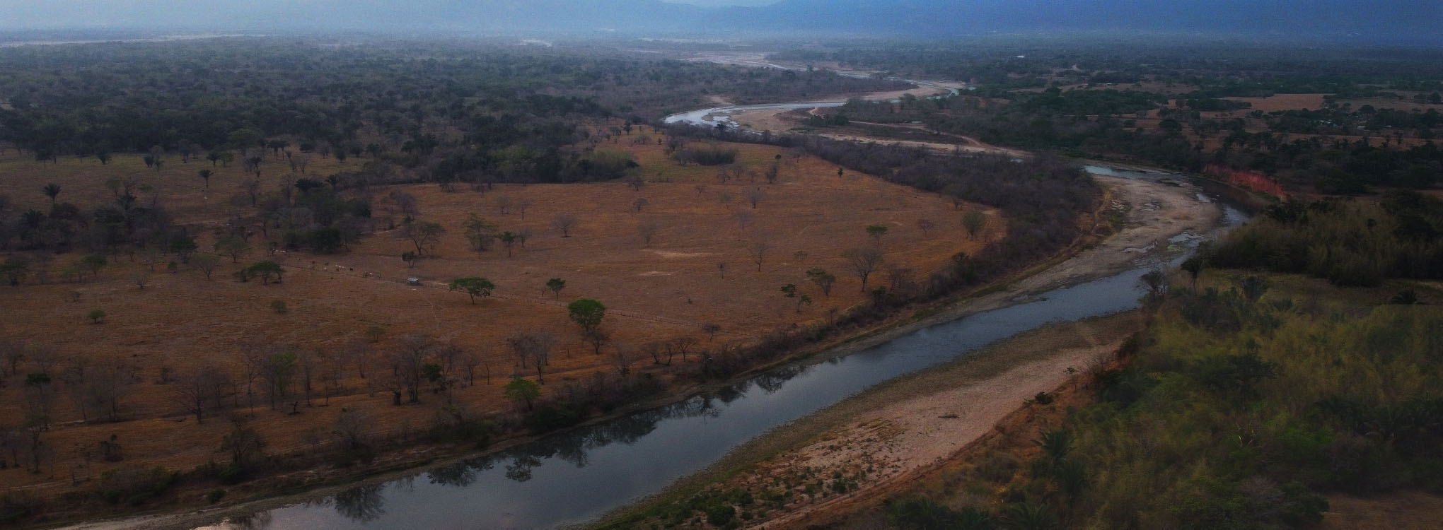 Vista aérea de un paisaje llanero con un río serpenteante, vegetación seca y montañas en el horizonte 