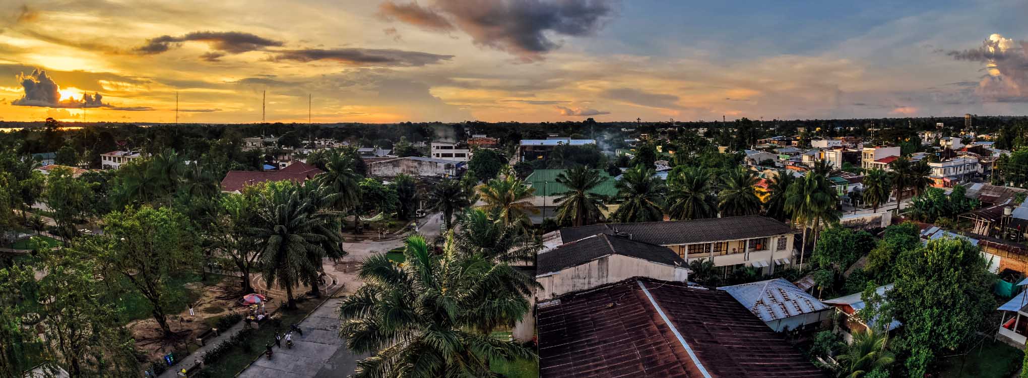 Vista panorámica al atardecer de la ciudad de Leticia, con palmeras, edificios y un cielo anaranjado.