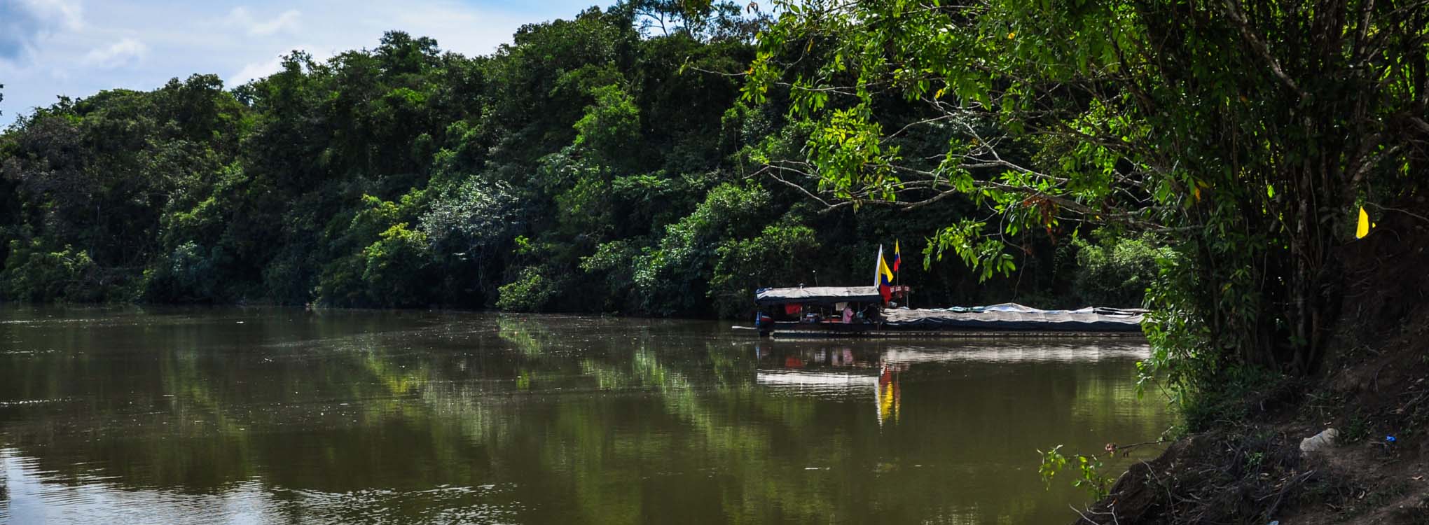 Río rodeado de vegetación exuberante con una embarcación que lleva la bandera de Colombia en Mitú.