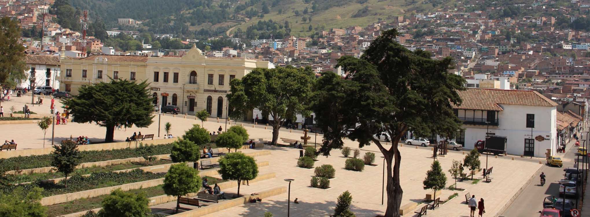 Plaza principal de una ciudad en Norte de Santander, rodeada de árboles, jardines y edificios.