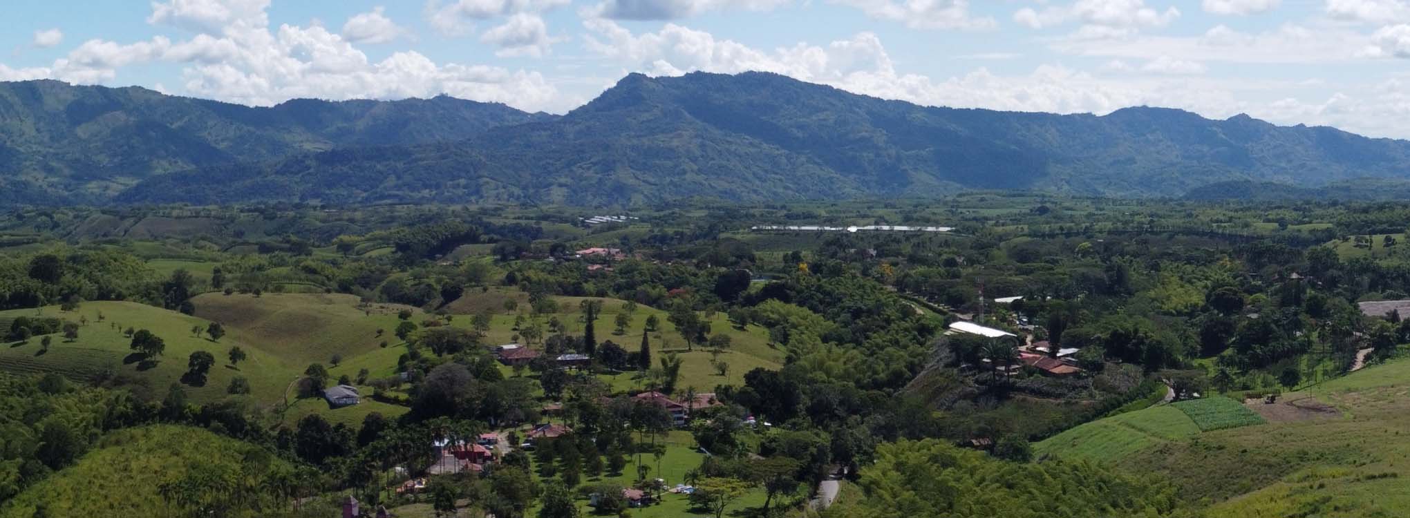 Vista panorámica de un paisaje montañoso en Risaralda, con colinas verdes, árboles dispersos y montañas en el horizonte.