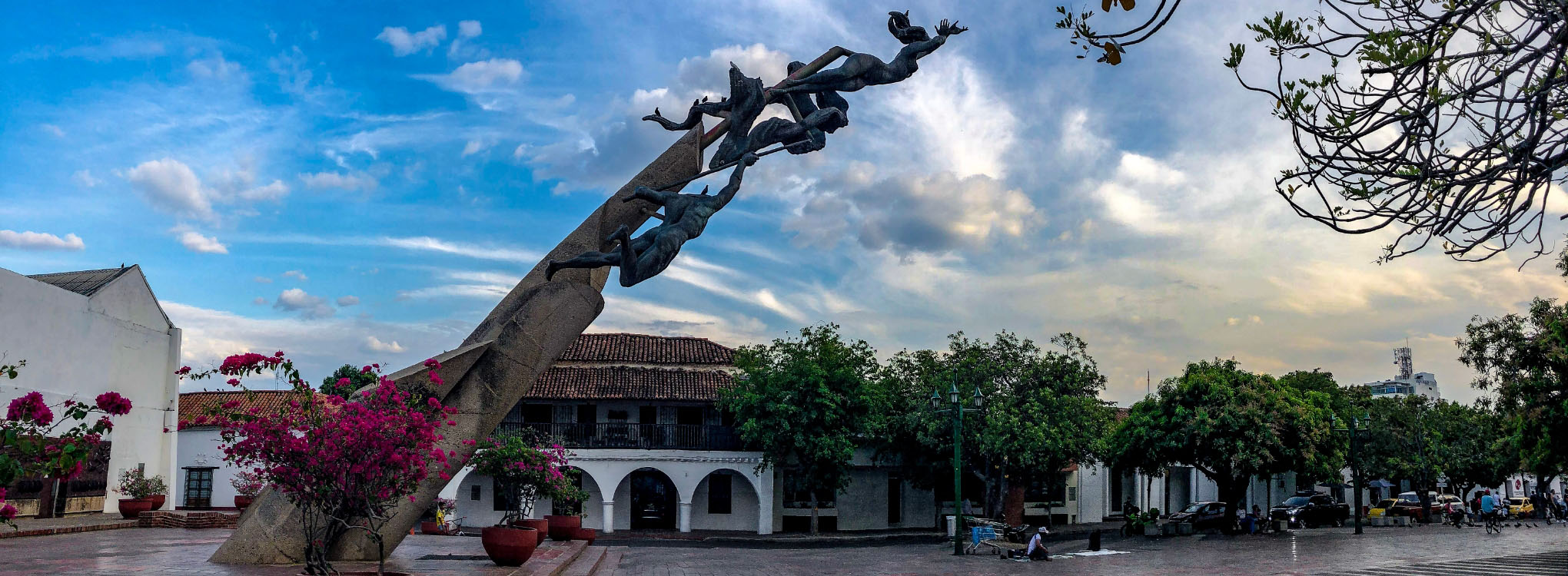 Monumento al Cacique Upar en una plaza de Valledupar, rodeado de vegetación y flores bajo un cielo parcialmente nublado.