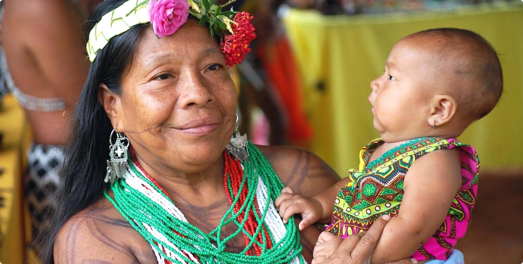 Mujer indígena sonriente con adornos tradicionales y un bebé en brazos