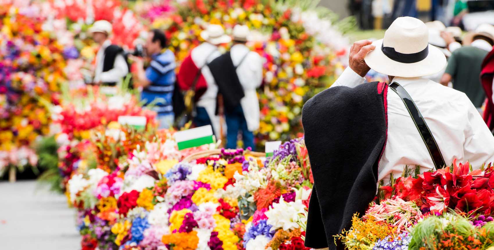 Hombre con sombrero blanco y ruana observando una colorida exhibición de flores