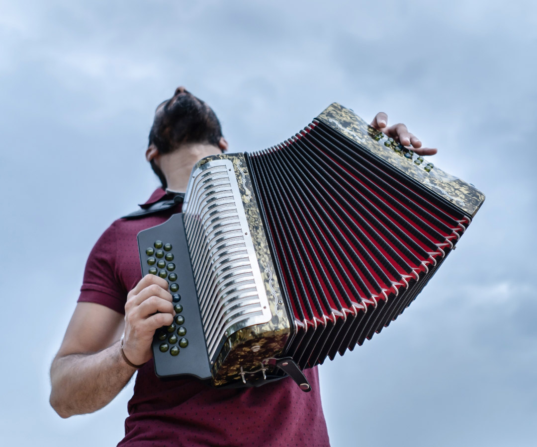 Hombre tocando un acordeón con una pose expresiva, bajo un cielo nublado.