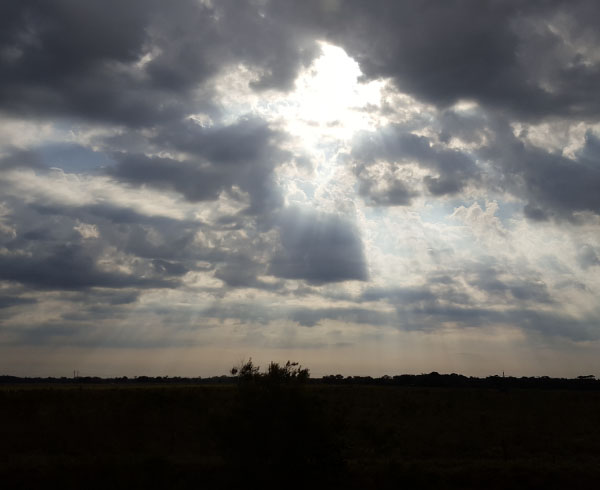 Cielo parcialmente nublado con rayos de sol atravesando las nubes, iluminando ligeramente el paisaje.