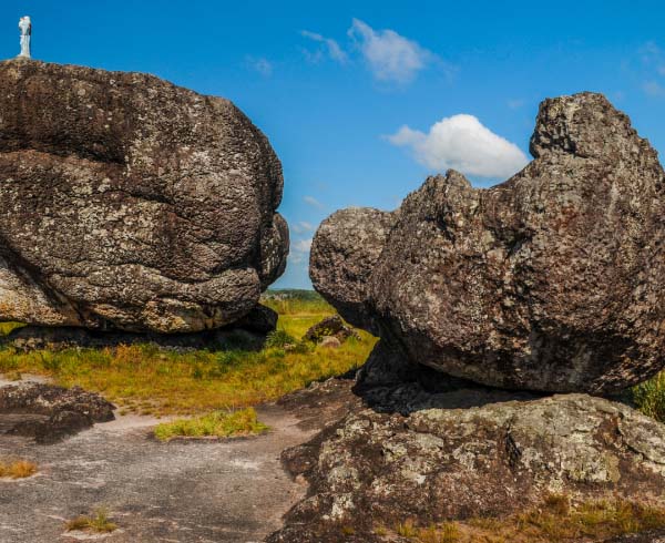 Formaciones rocosas imponentes en un paisaje abierto con una estatua en la cima de una de las rocas.