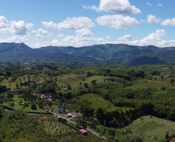 Vista panorámica de un paisaje montañoso en Risaralda, con colinas verdes, árboles dispersos y montañas en el horizonte.