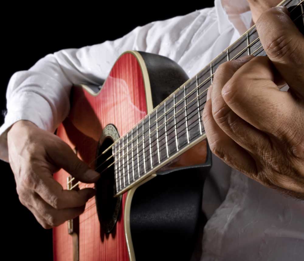 Primer plano de las manos de un hombre tocando una guitarra acústica.