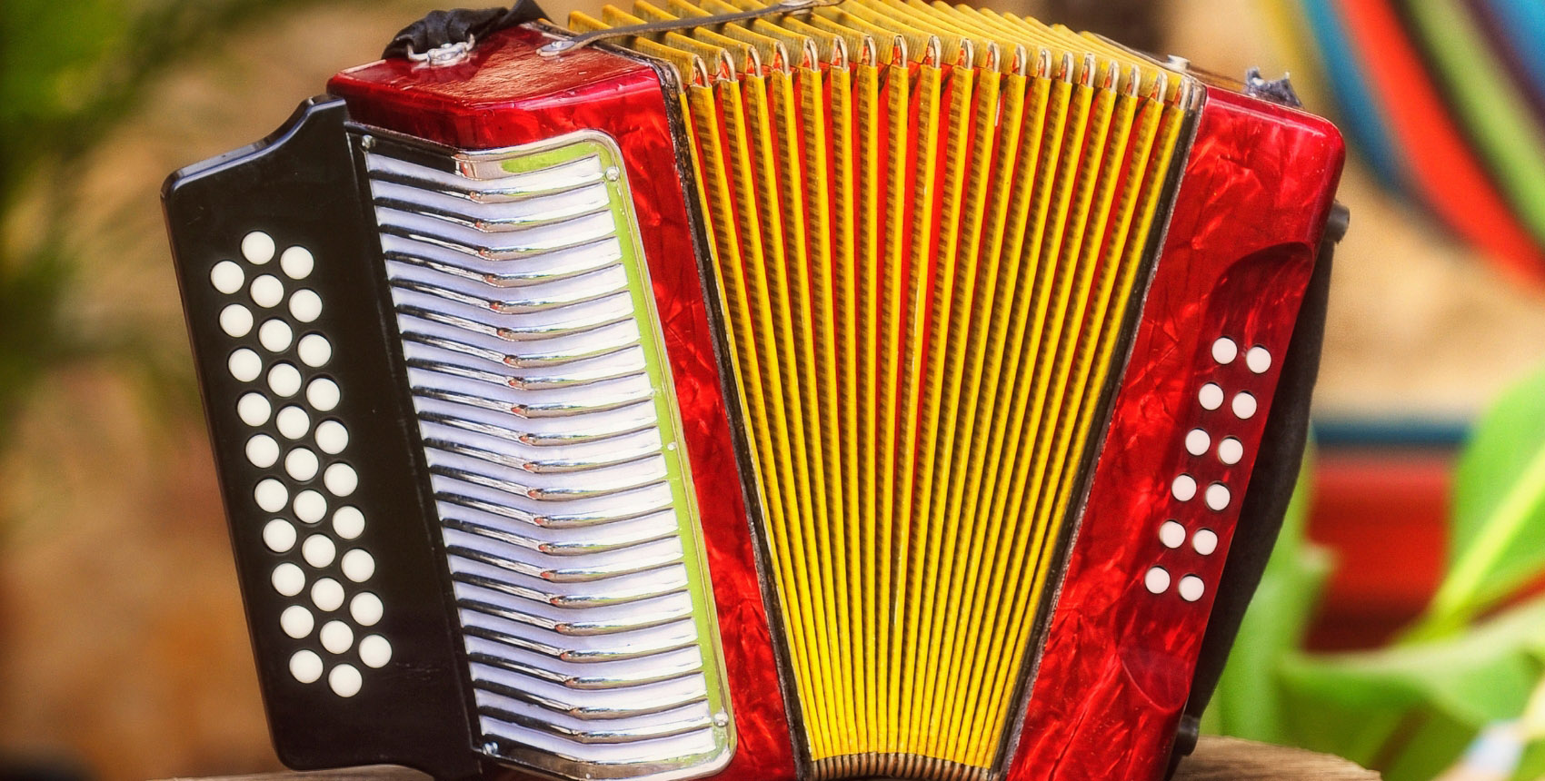 Red accordion with yellow and black details, typical instrument of vallenata music, placed on a wooden surface.