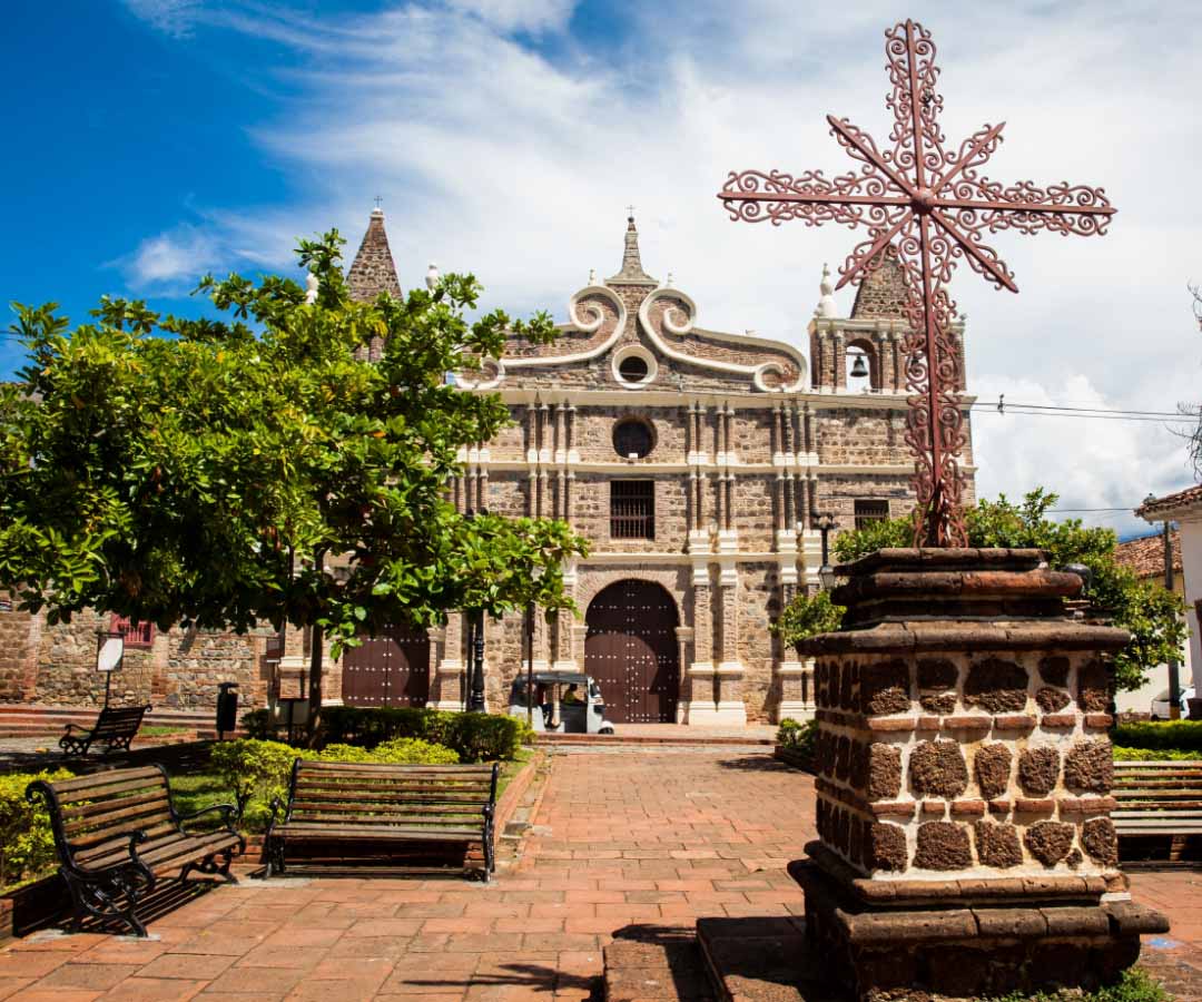 Iglesia colonial en Risaralda, rodeada de un parque con bancas y árboles.