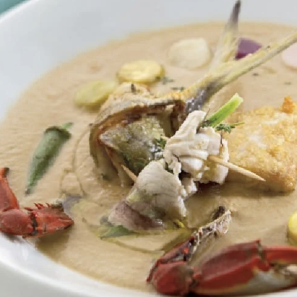 Dish of rondón, a traditional Caribbean soup with fish, crab, vegetables and plantain chunks, served in a white bowl.