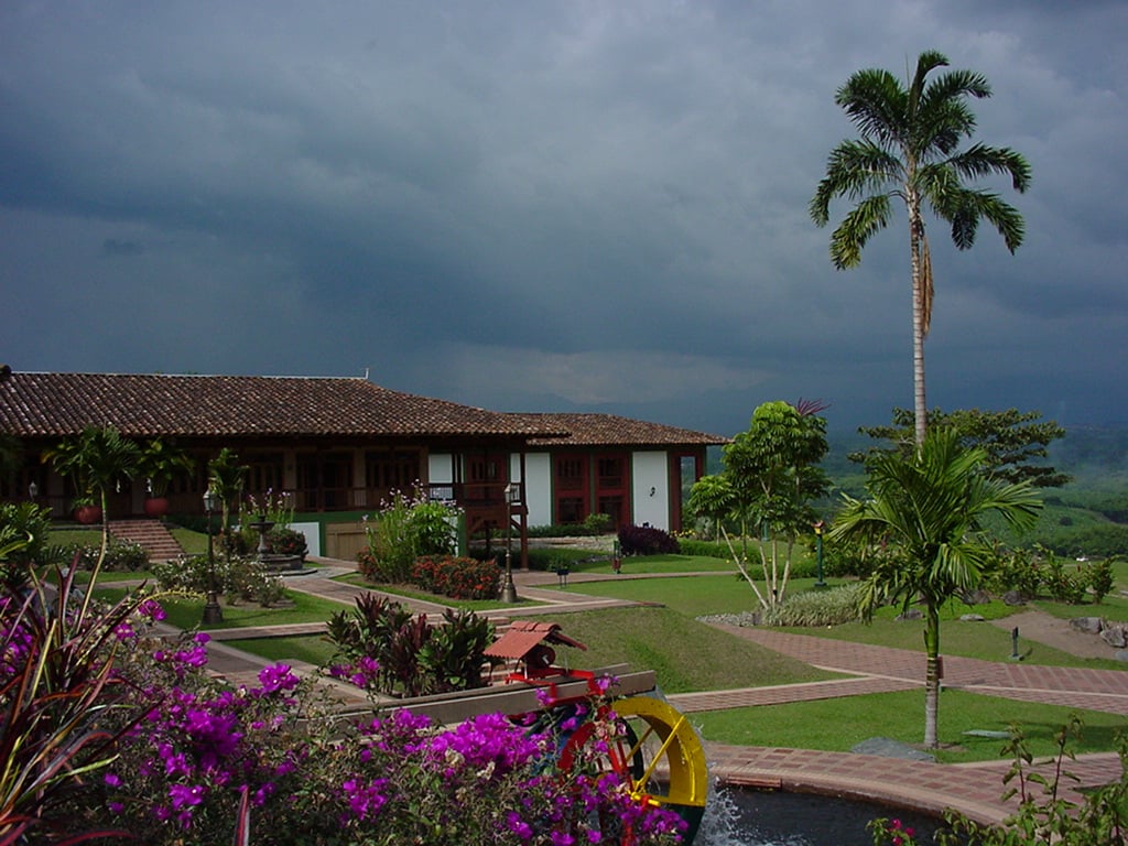 Hacienda colonial con jardín y cielo nublado.