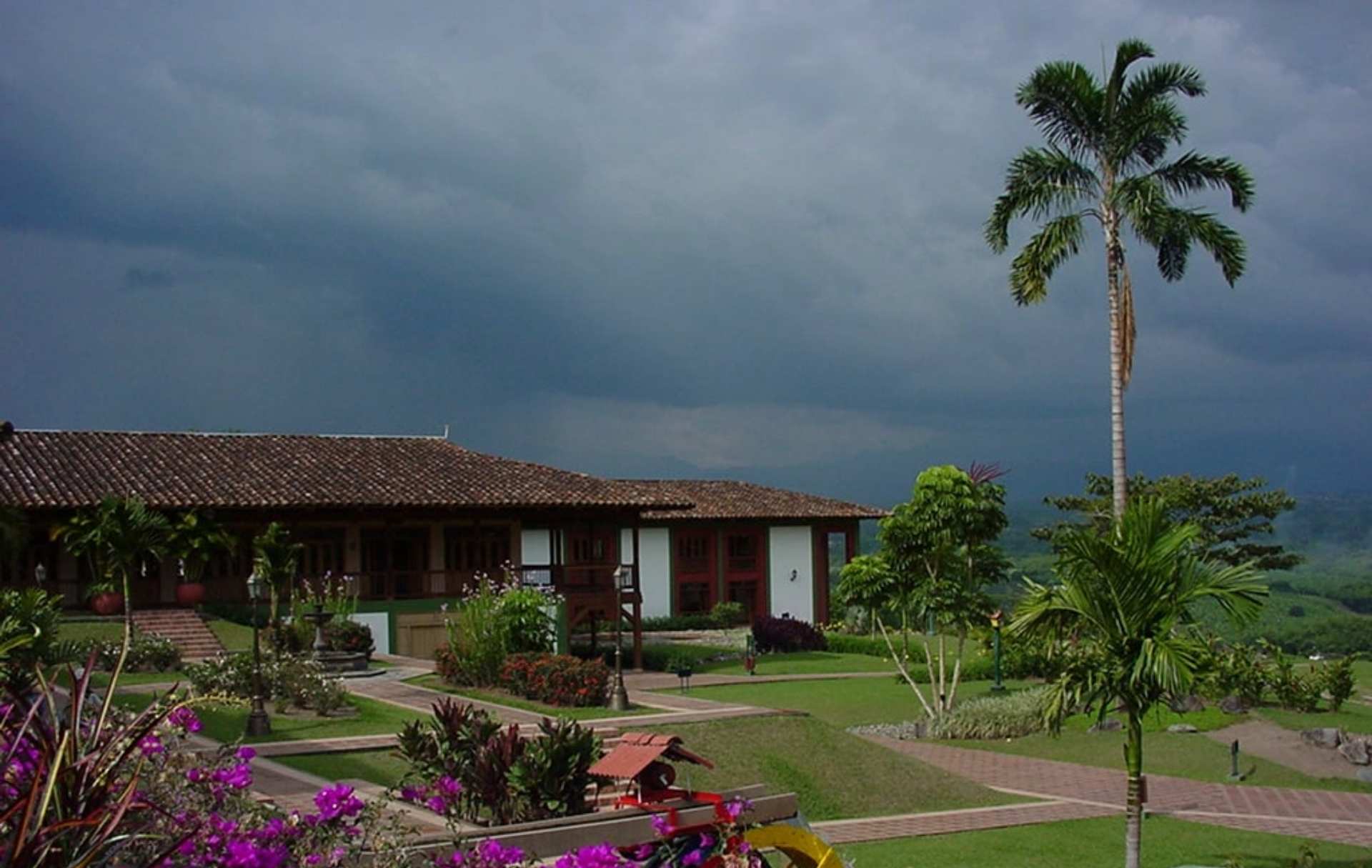 Hacienda típica del Eje Cafetero colombiano, rodeada de jardines coloridos y palmeras.