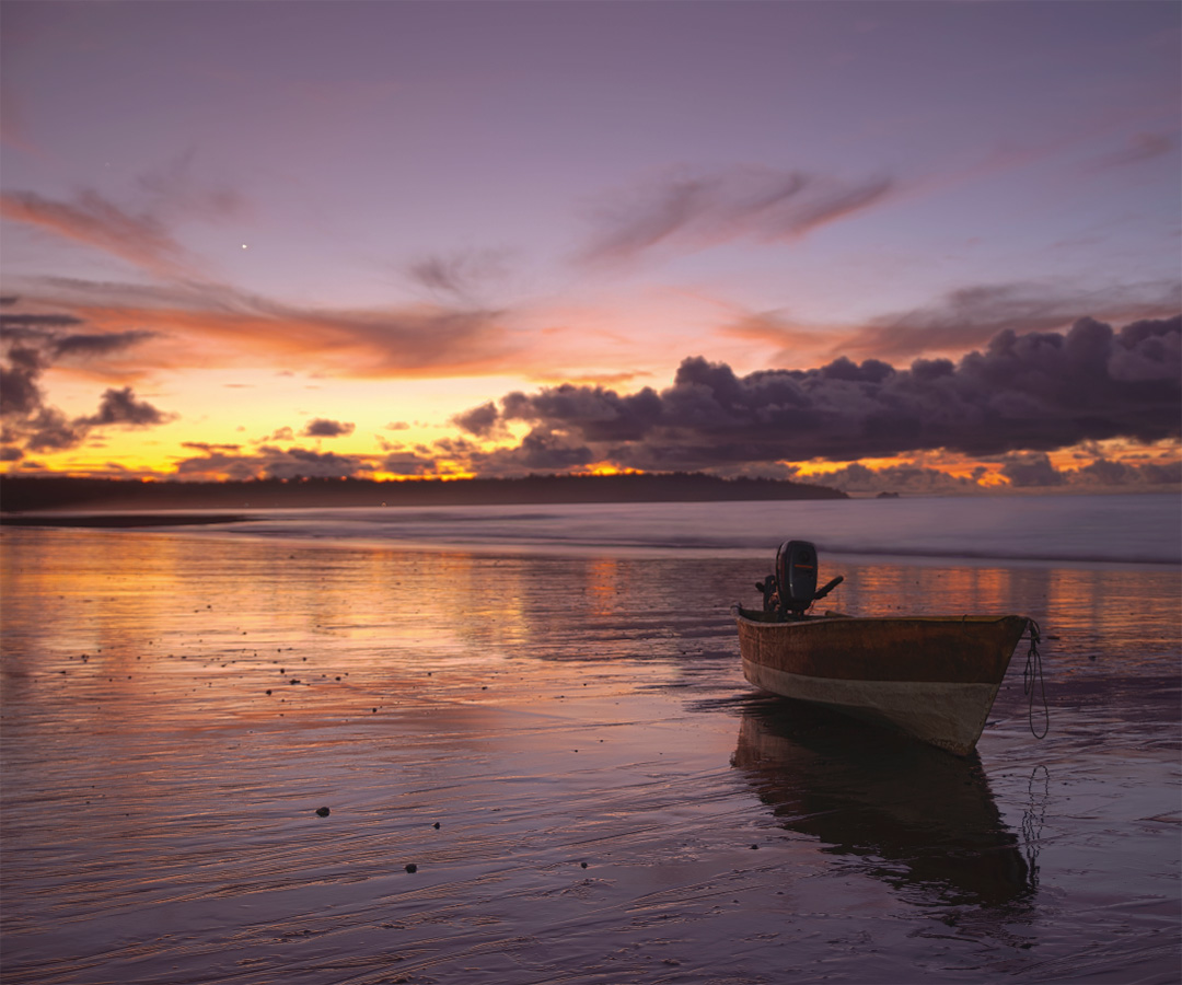 Atardecer en la costa de Quibdó, con un bote reflejándose en la arena húmeda, mientras el cielo se tiñe de tonos cálidos.