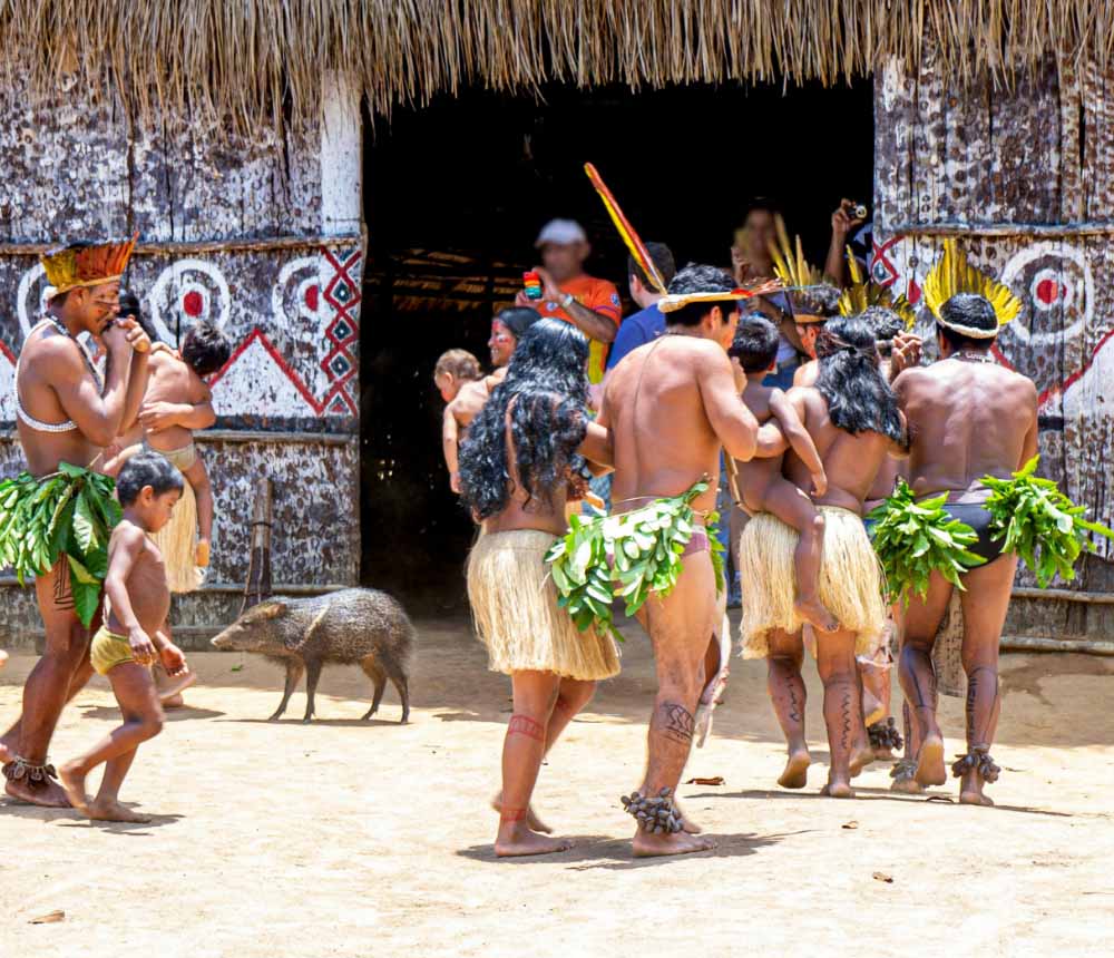 Grupo de personas indígenas en un ritual cultural, vistiendo trajes tradicionales hechos de hojas y fibras naturales.