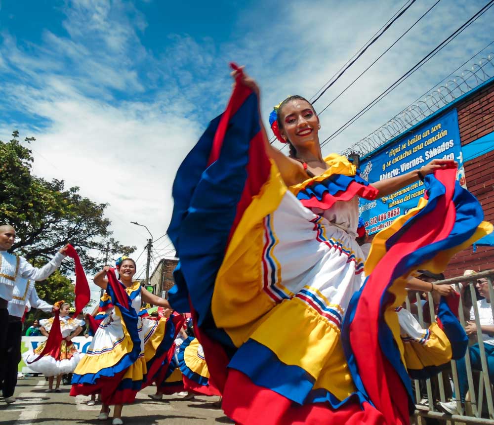 Bailarina con traje típico colombiano en un desfile al aire libre, mostrando los colores de la bandera de Colombia.