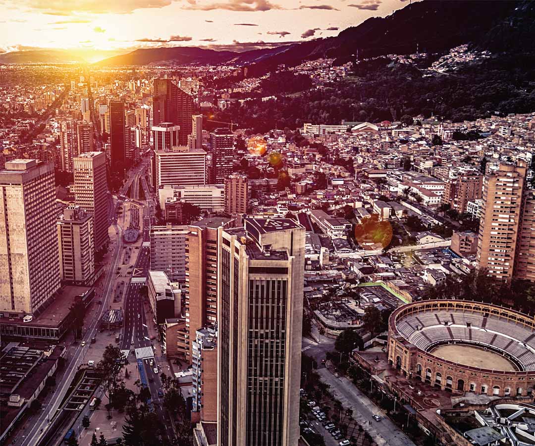 Panorámica de Bogotá al atardecer, destacando edificios modernos, la Plaza de Toros de Santamaría.