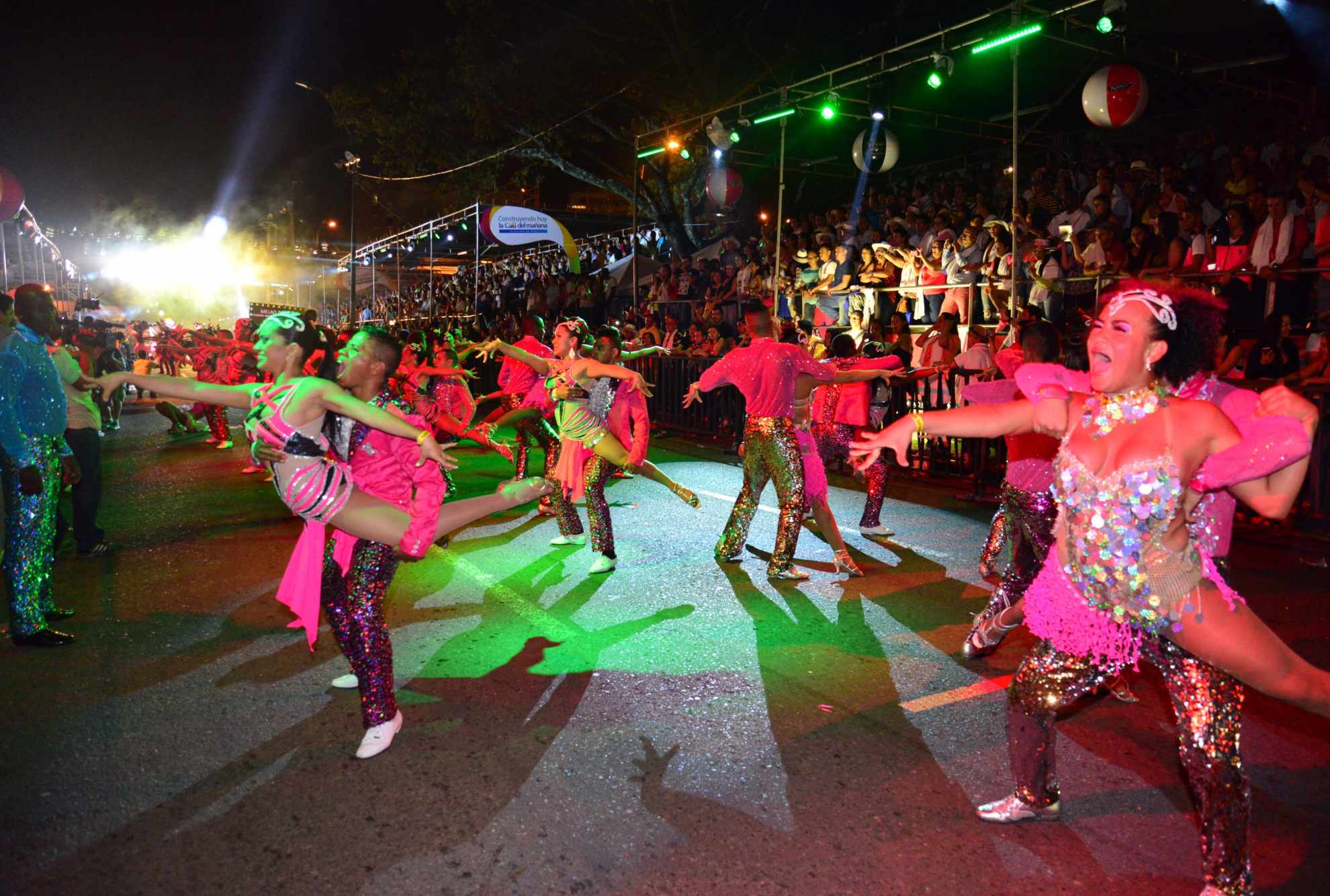 Grupo de bailarines en un desfile nocturno con trajes coloridos y brillantes.