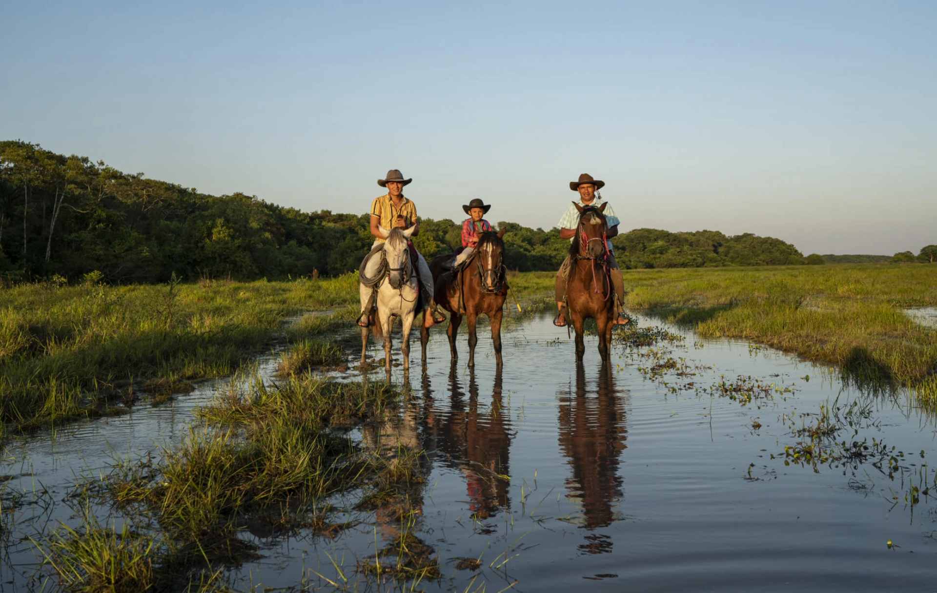 Tres llaneros a caballo cruzando un paisaje inundado en los Llanos Orientales