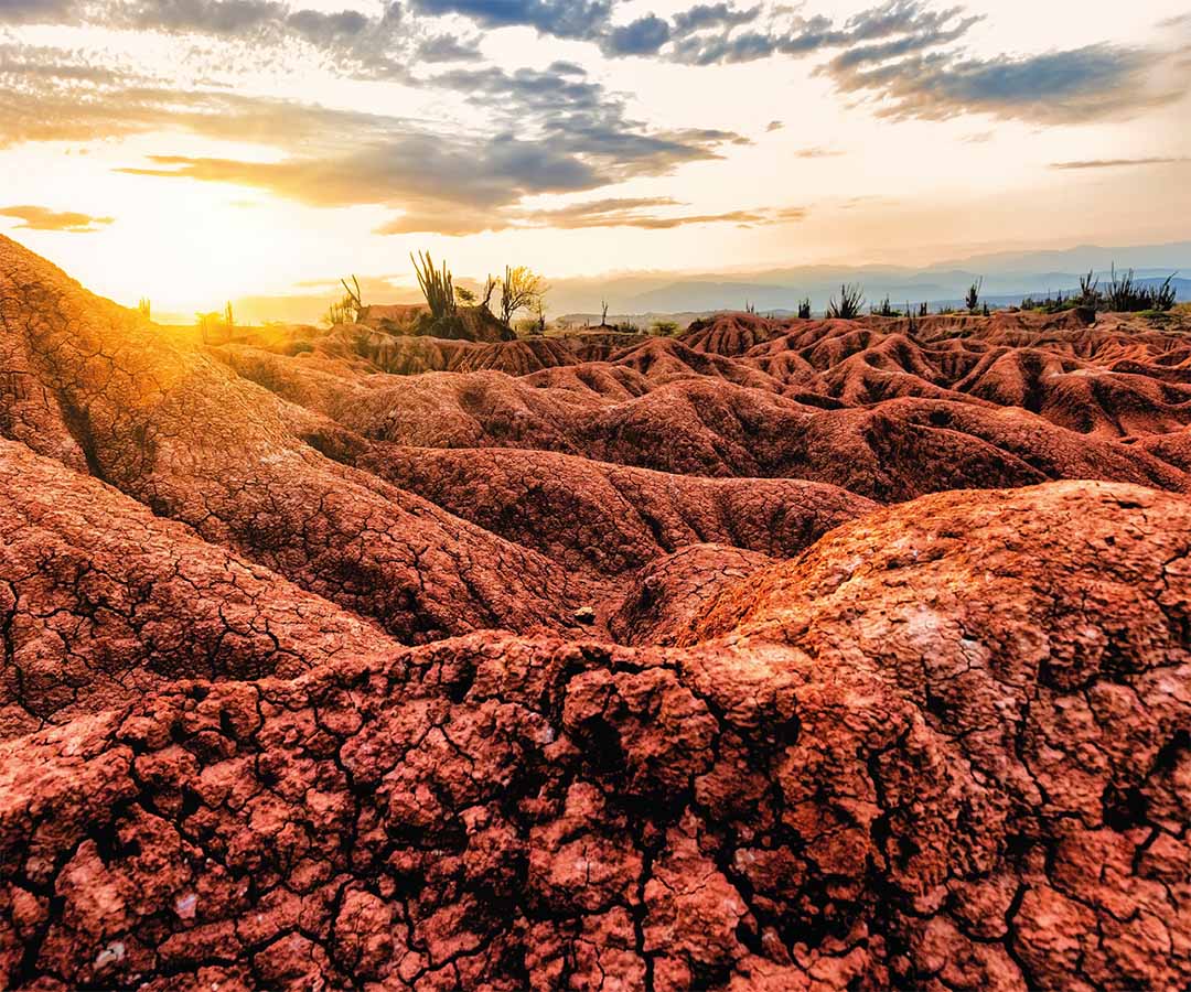 Paisaje del Desierto de la Tatacoa cerca de Neiva, con formaciones de tierra rojiza y un atardecer.