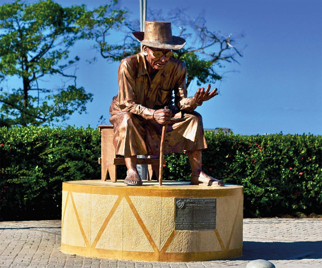 Escultura de Francisco el Hombre en Riohacha, sentado con sombrero y bastón, representando la tradición vallenata.