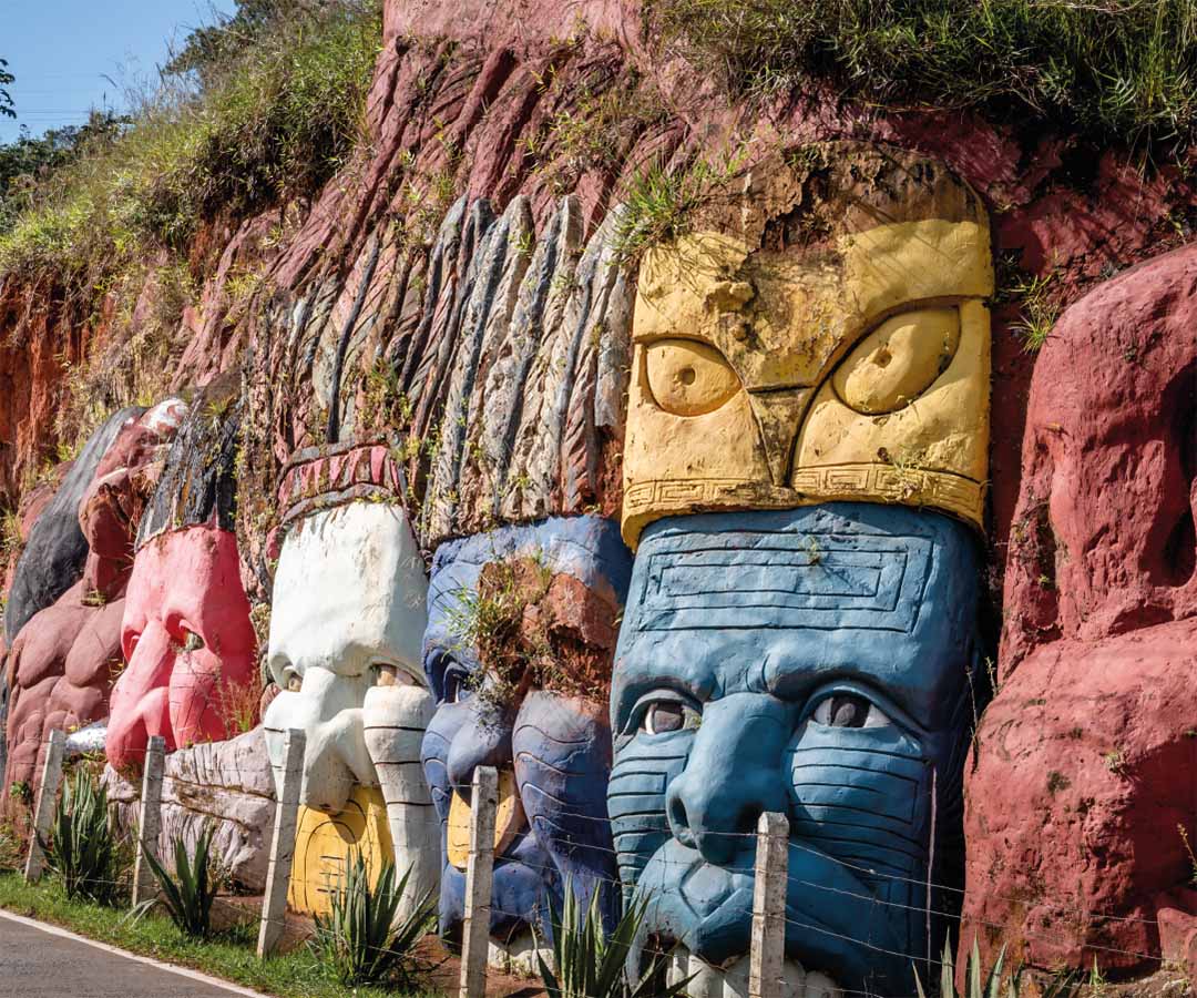 Esculturas de rostros tallados en una pared de roca en Cali, con colores vivos y diseños que reflejan la cultura ancestral.