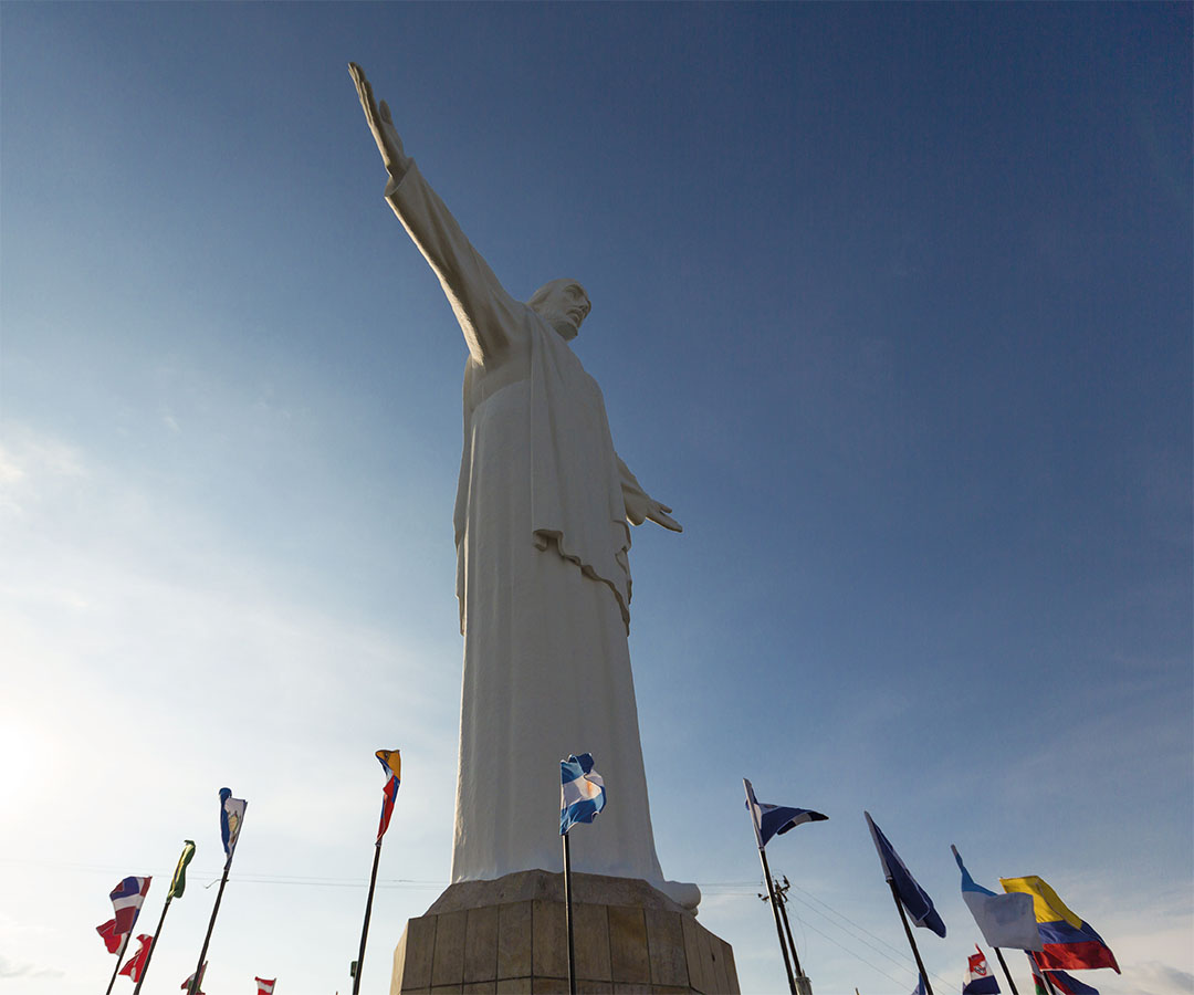 Estatua del Cristo Rey en Cali, imponente bajo un cielo despejado, rodeada de banderas.