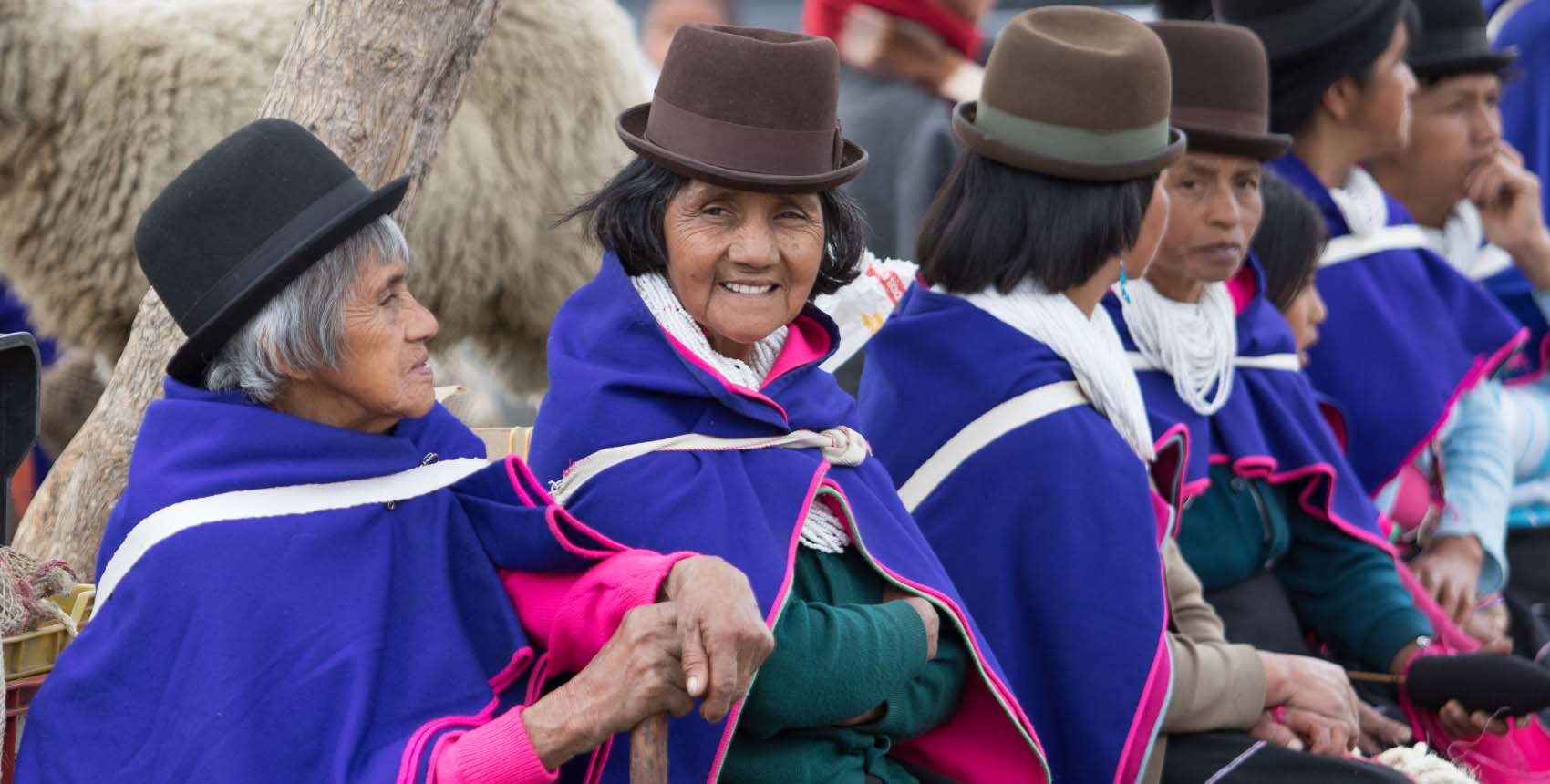 Mujeres indígenas vestidas con ponchos tradicionales de color azul y sombreros, reunidas en un ambiente comunitario.