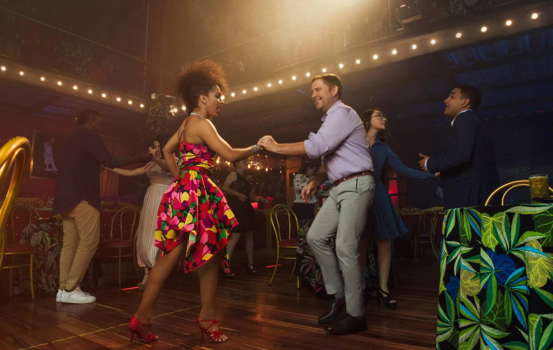 Pareja bailando salsa en un club nocturno con decoración tropical.