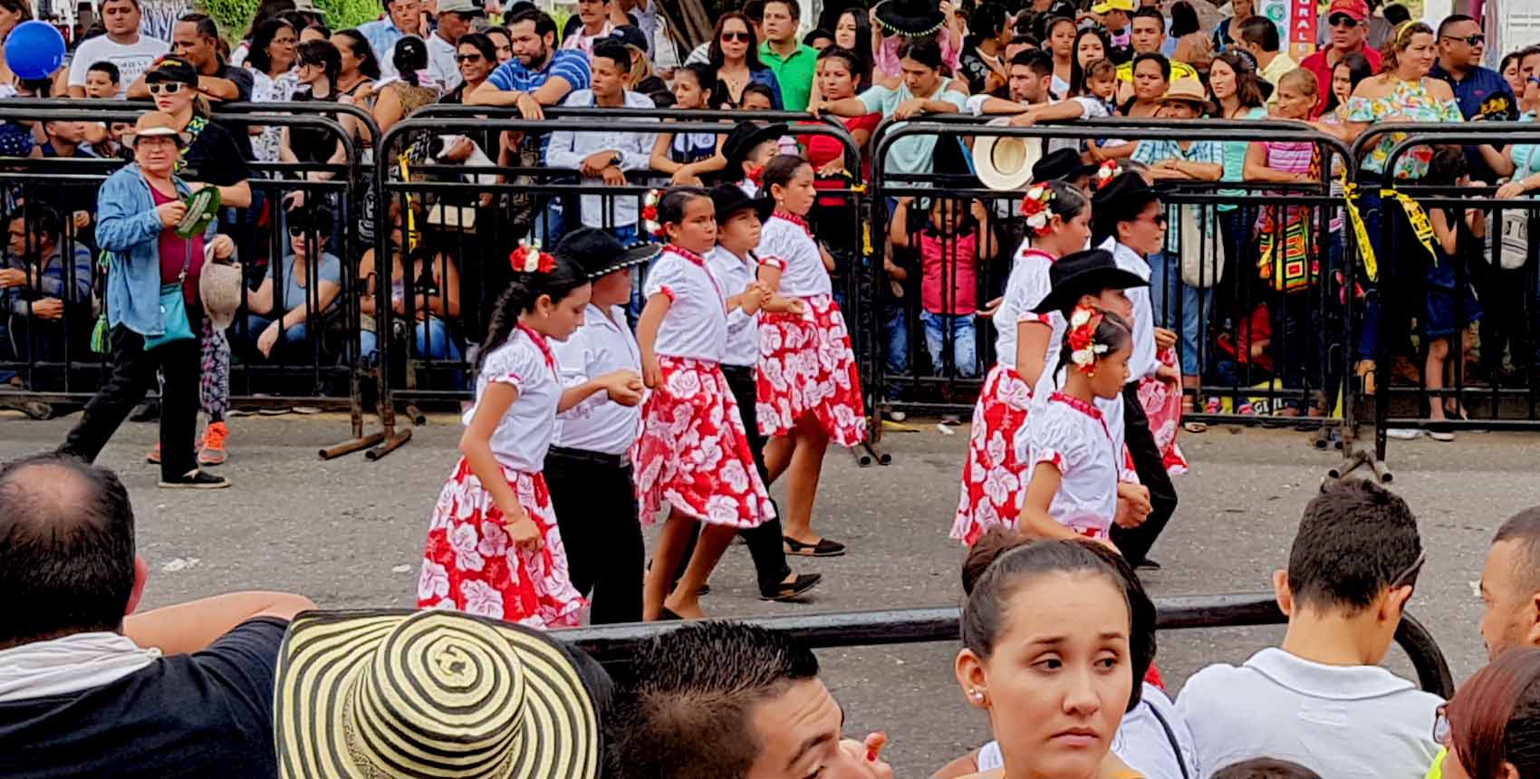 Niños vestidos con trajes típicos colombianos participando en un desfile cultural.