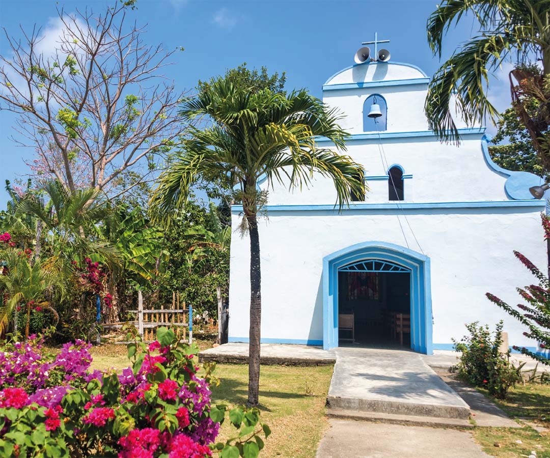 Iglesia blanca con detalles azules en Quibdó, rodeada de palmeras, flores coloridas y vegetación.