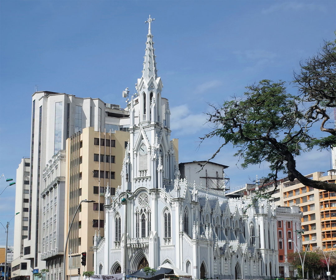 Iglesia La Ermita en Cali, destacando su estilo gótico con detalles blancos, rodeada de edificios modernos y un cielo despejado.