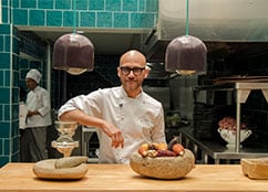 Chef posando detrás de una mesa de madera con utensilios y alimentos frescos