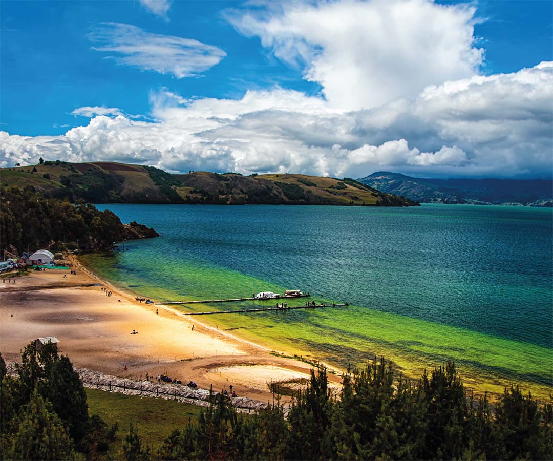 Vista panorámica de la playa Blanca en el lago de Tota, Boyacá, Colombia, con aguas cristalinas, arena dorada y colinas verdes.