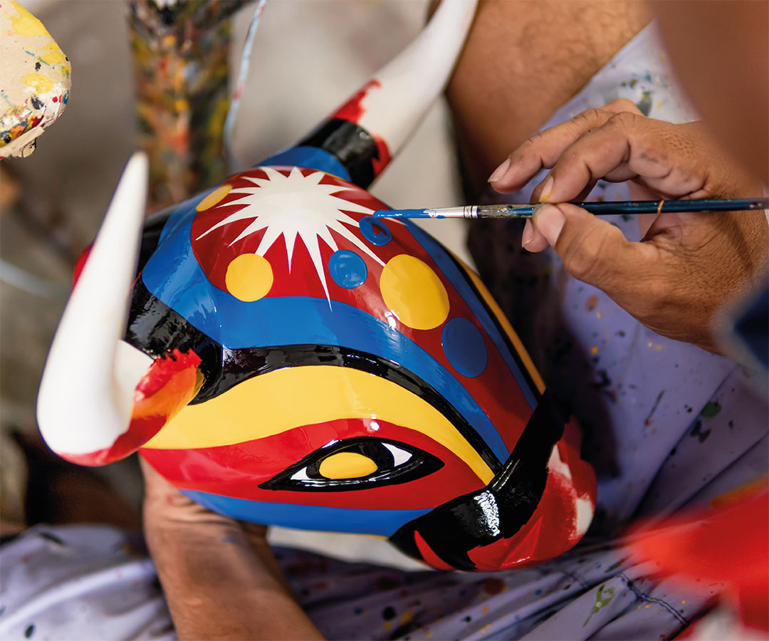 Manos pintando una máscara colorida con diseño tradicional.