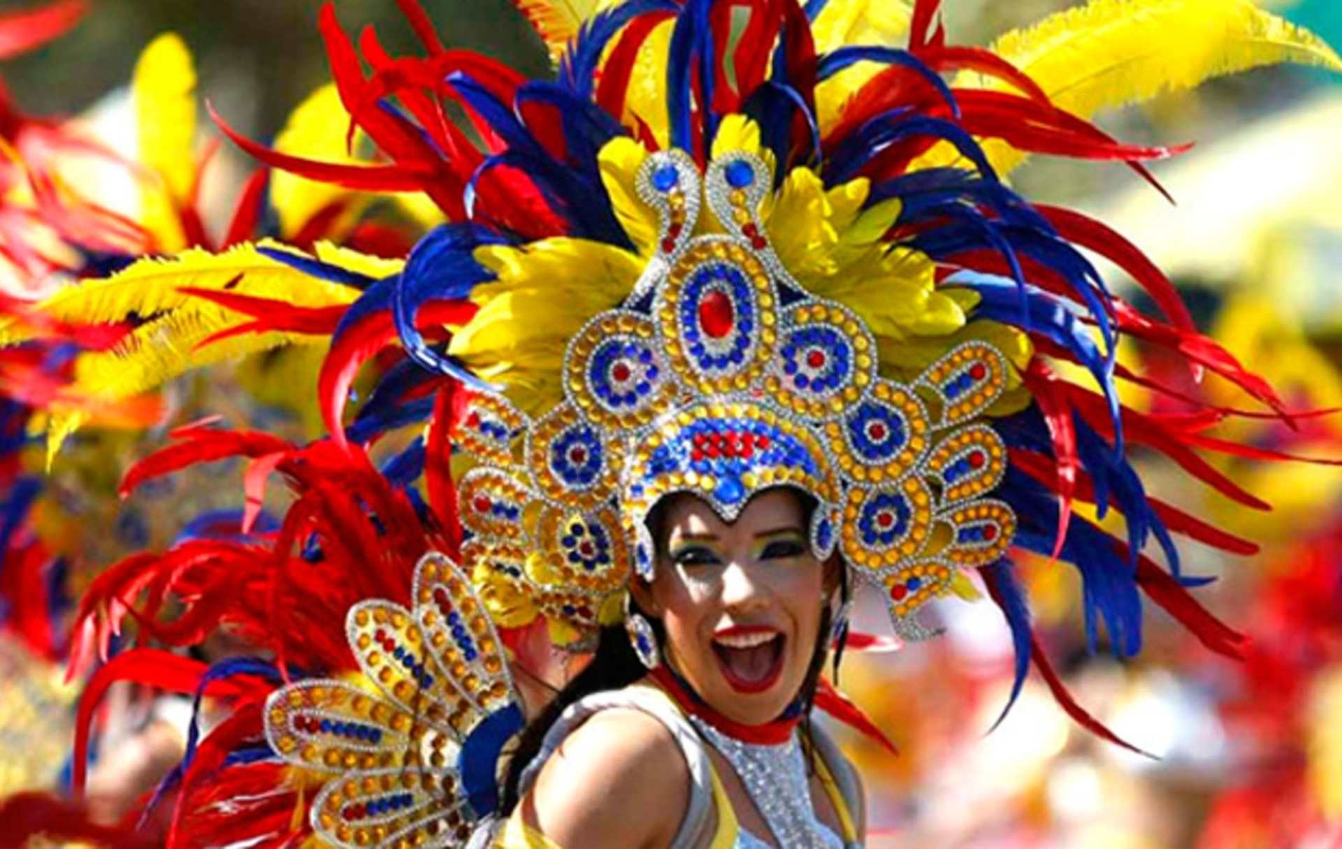 Mujer sonriente con un colorido disfraz y tocado decorado con plumas rojas, amarillas y azules, representando el espíritu vibrante de un carnaval.