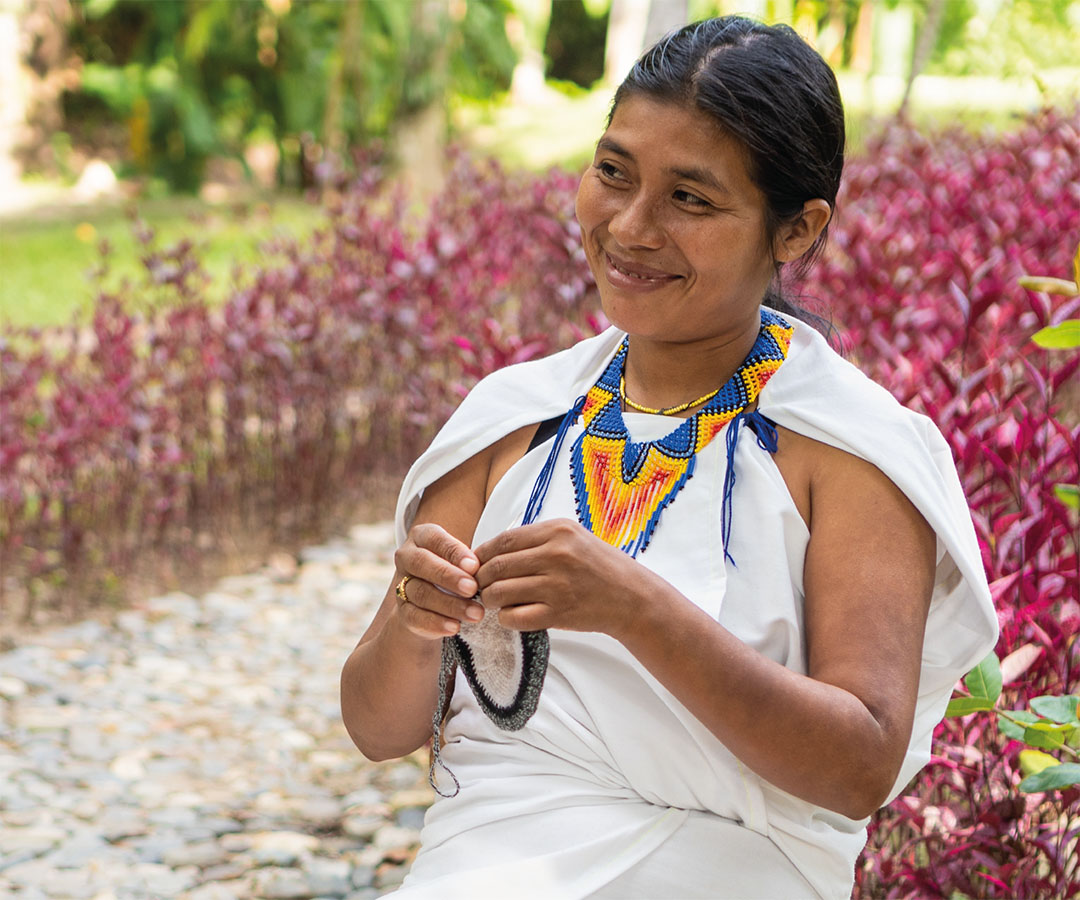 Mujer indígena en Santa Marta tejiendo con una sonrisa.