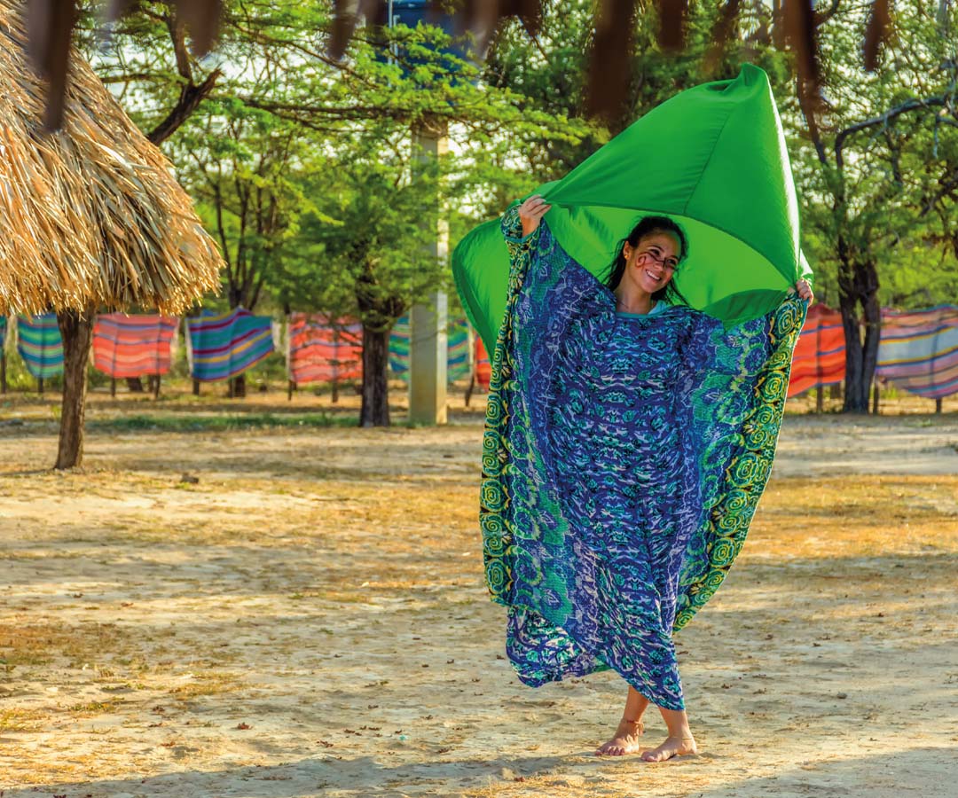 Mujer sonriente en Riohacha sosteniendo una manta verde y vistiendo un vestido tradicional.