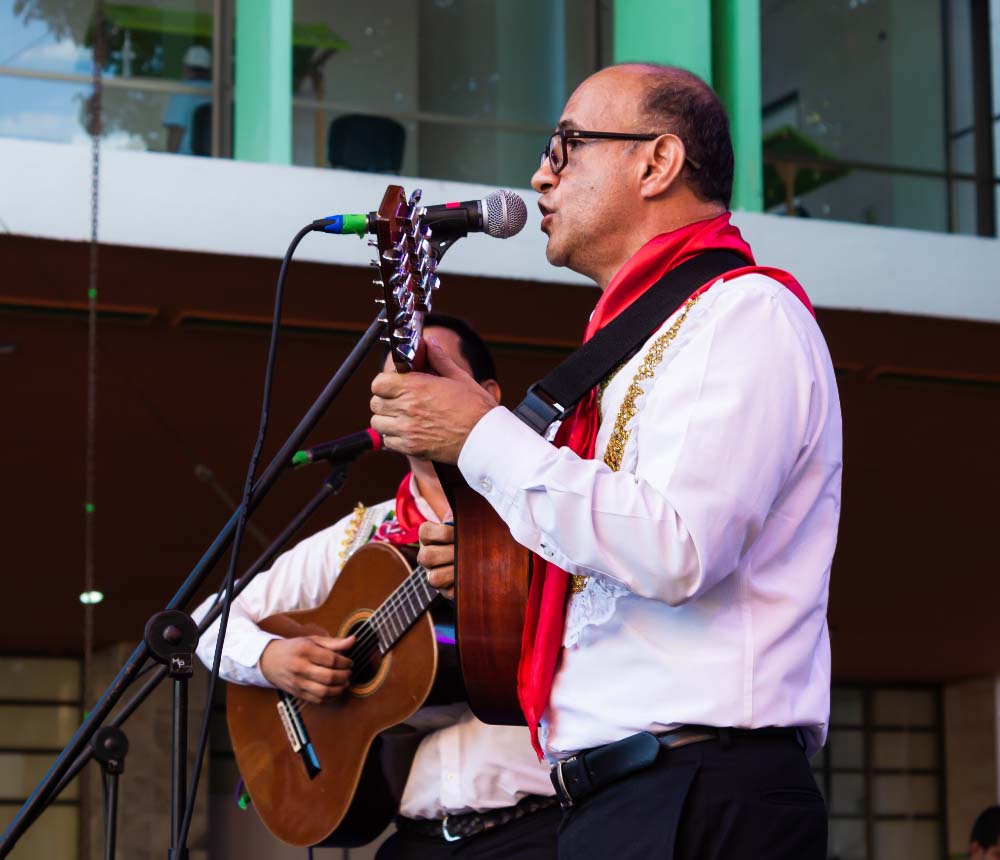 Músico vestido con traje tradicional, tocando una guitarra y cantando frente a un micrófono durante una presentación