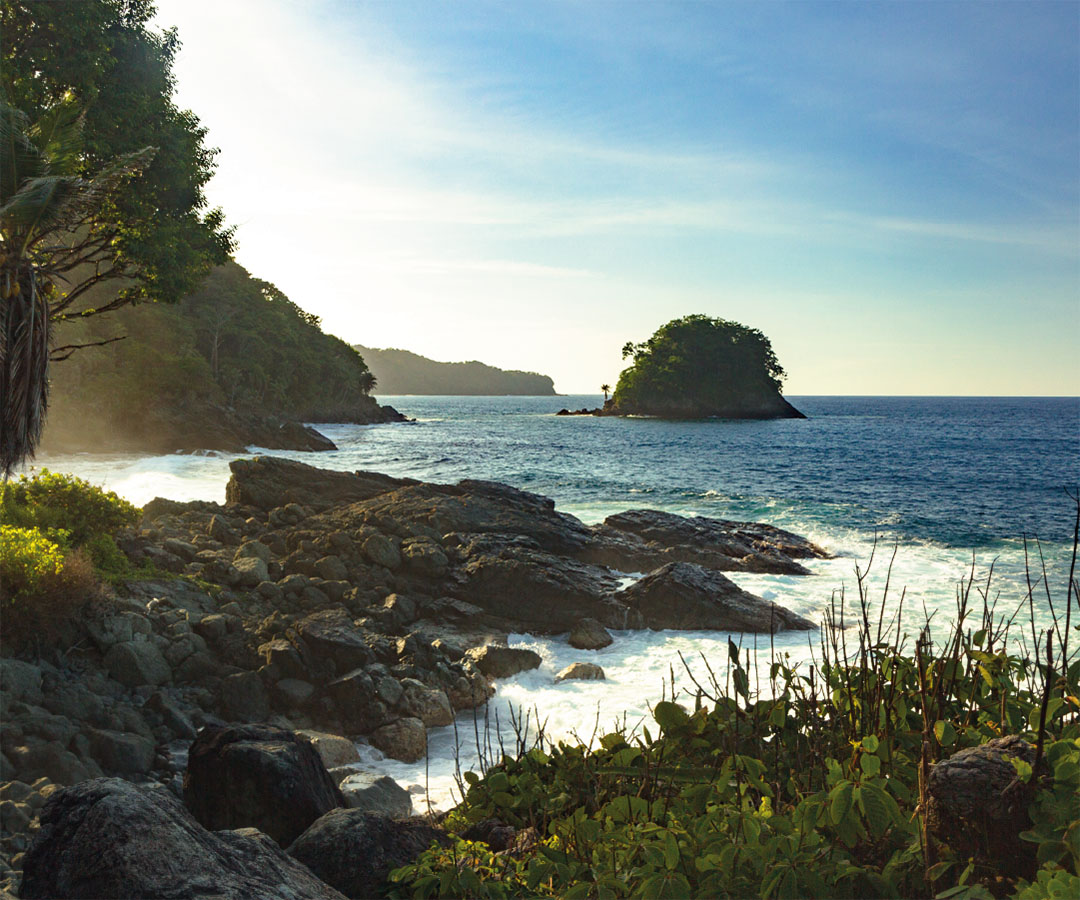 Paisaje costero en Quibdó, con rocas, vegetación tropical y pequeñas islas en el horizonte, bajo un cielo despejado.