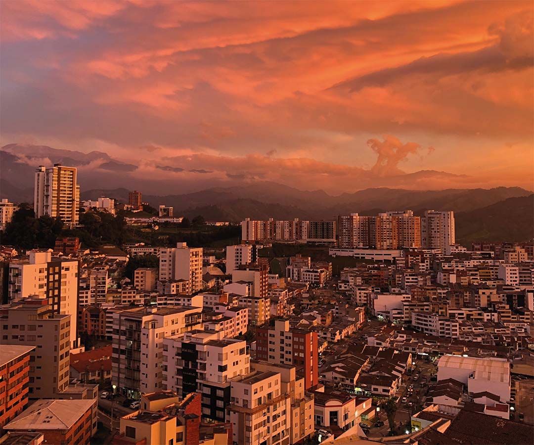 Vista panorámica de Manizales al atardecer, con un cielo teñido de colores cálidos que resaltan su paisaje urbano.