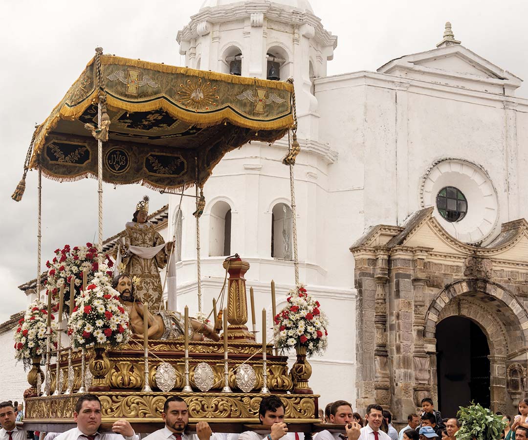 Procesión religiosa en Popayán con una imagen sagrada decorada con flores y ornamentos, frente a una iglesia blanca.